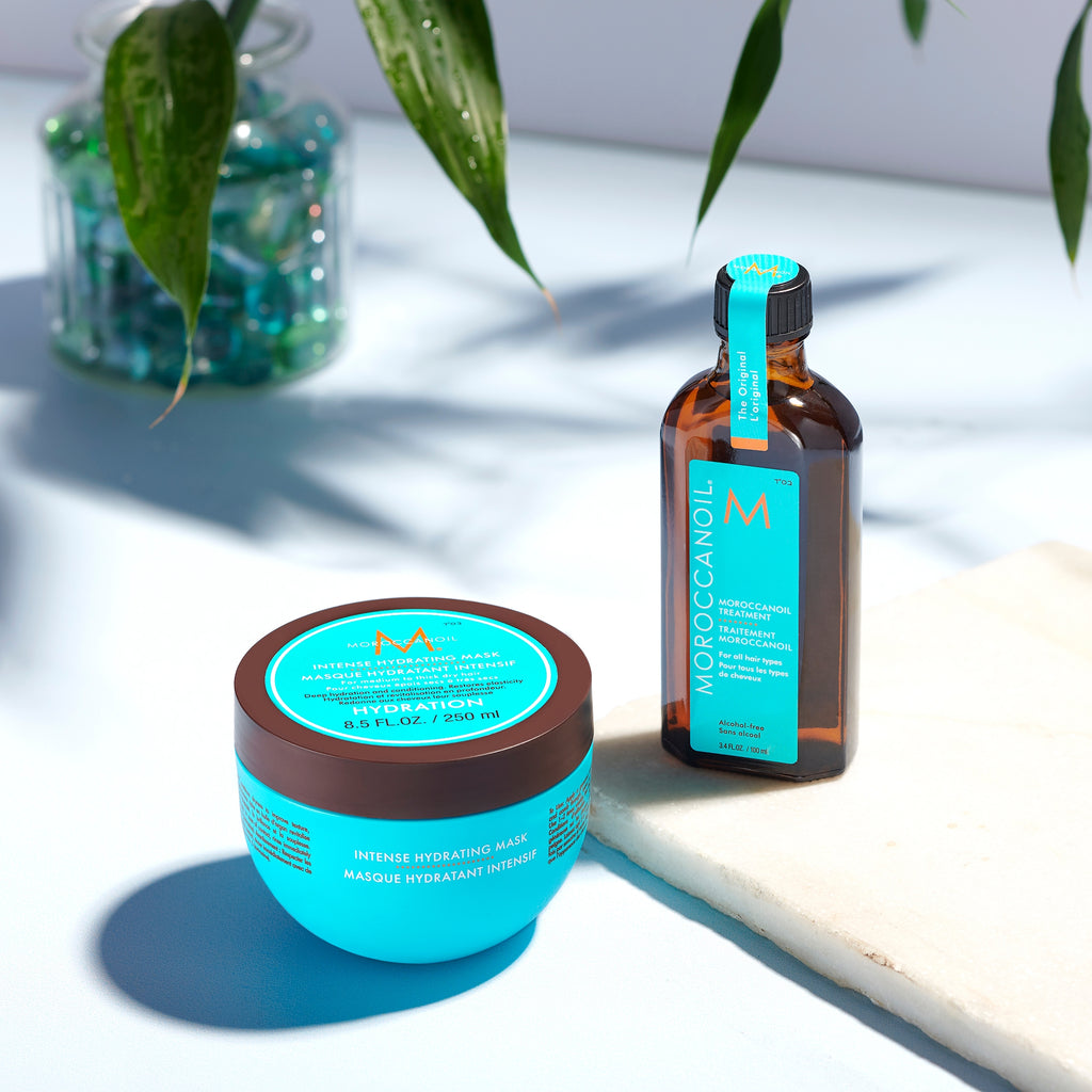 Moroccanoil hair care products on a light surface with green leaves in the background