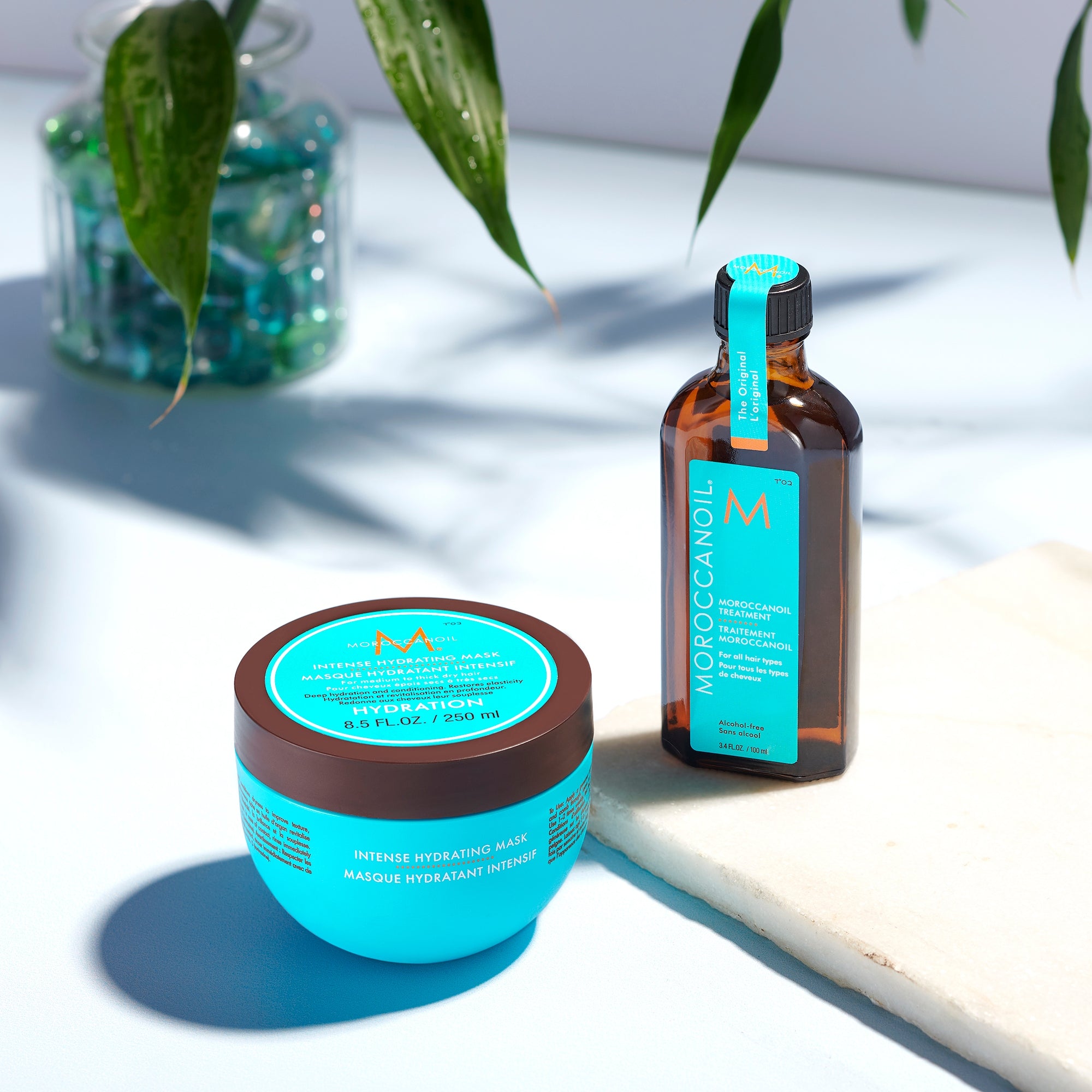 Moroccanoil hair care products on a light surface with green leaves in the background