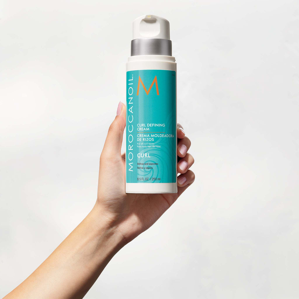 Hand holding a bottle of Moroccanoil Curl Defining Cream against a white background